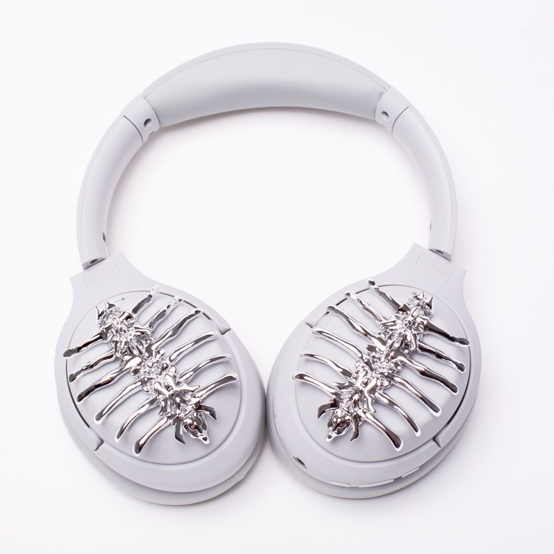 May include: Gray over-ear headphones with silver decorative accents on the earcups. The accents are in the shape of a stylized skeletal design.