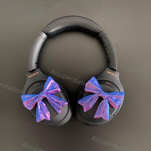 May include: Black wireless headphones with a purple and blue bow on each earcup. The headphones have the word "SONY" printed on each earcup.