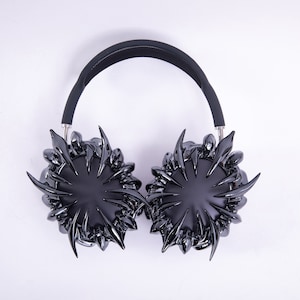May include: Black headphones with a unique design featuring a spiky, starburst-like pattern on the earcups.