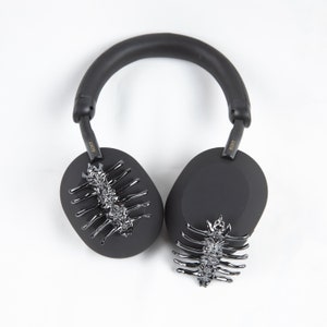 May include: Black over-ear headphones with a silver decorative design on each earcup. The headphones have a black headband and the word "SONY" is written in gold on each earcup.