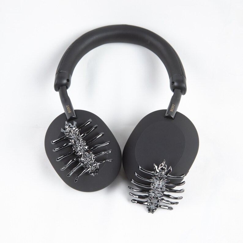 May include: Black over-ear headphones with a silver decorative design on each earcup. The headphones have a black headband and the word "SONY" is written in gold on each earcup.