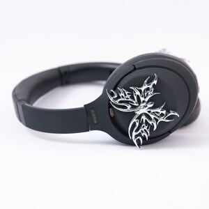 May include: Black wireless headphones with a silver butterfly design on the earcup. The headphones have a black headband and earcups with the word "SONY" printed on the side.