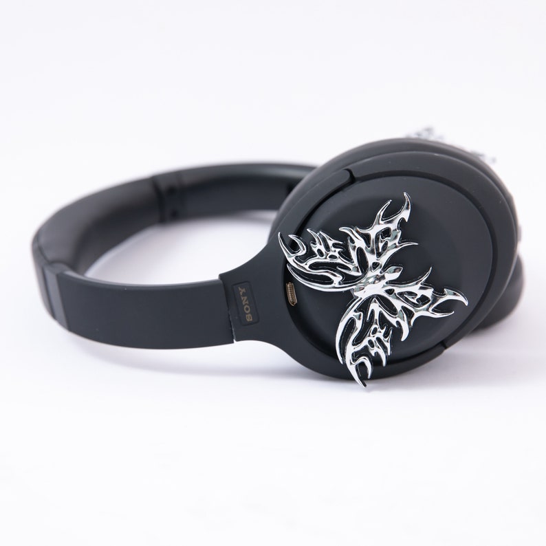 May include: Black wireless headphones with a silver butterfly design on the earcup. The headphones have a black headband and earcups with the word "SONY" printed on the side.