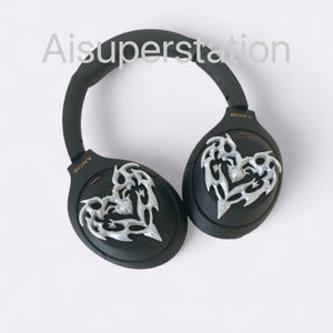 May include: Black wireless headphones with a silver heart design on each earcup. The headphones have the word "SONY" printed on each earcup.