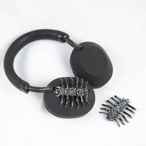 May include: Black over-ear headphones with a gold "SONY" logo on each earcup. The headphones are decorated with a black metal scorpion design on each earcup.