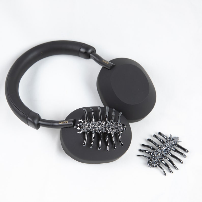 May include: Black over-ear headphones with a gold "SONY" logo on each earcup. The headphones are decorated with a black metal scorpion design on each earcup.
