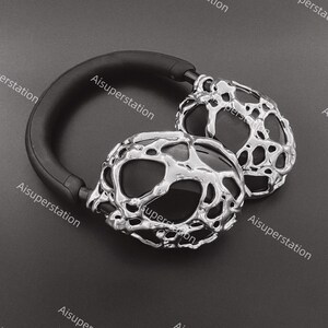 May include: A pair of black headphones with silver, textured earcups. The earcups have a unique, organic, and abstract design.