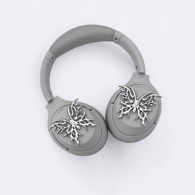 May include: Gray wireless headphones with a silver butterfly design on each earcup.
