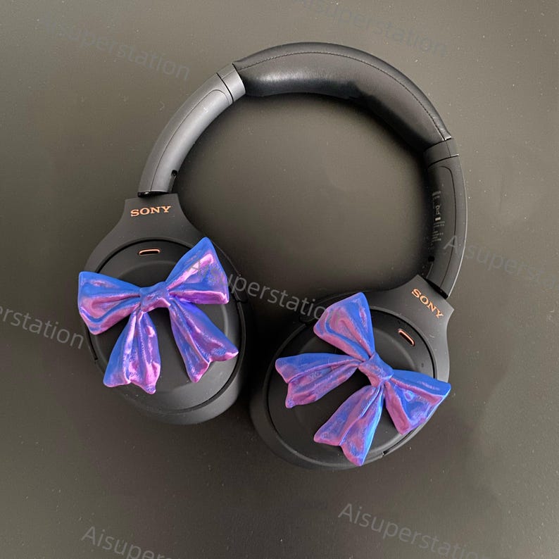 May include: Black over-ear headphones with a blue and purple iridescent bow on each earcup. The headphones have the word "SONY" printed on each earcup.
