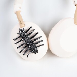 May include: Cream-colored headphones with a black, spidery design on one ear cup. The brand name "SONY" is visible on the headband. The headphones have a modern, minimalist aesthetic.
