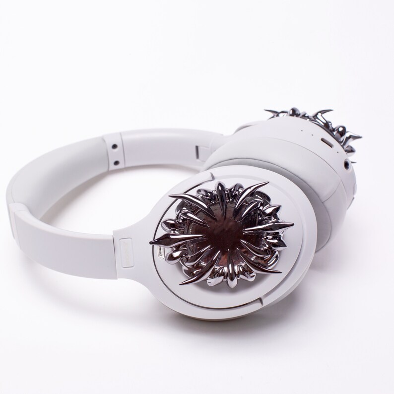 May include: White wireless headphones with a silver, spiky, starburst design on one earcup.