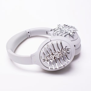May include: Gray over-ear headphones with a silver decorative design on each earcup. The design resembles a stylized skeletal structure with intricate details.