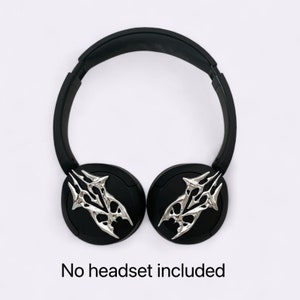 Puede incluir: Auriculares inal&aacute;mbricos negros con detalles decorativos plateados en las almohadillas. No se incluye ning&uacute;n auricular.