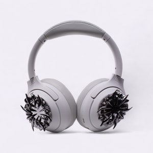 May include: Gray wireless headphones with black metal accents on the earcups. The accents are in the shape of a stylized starburst.