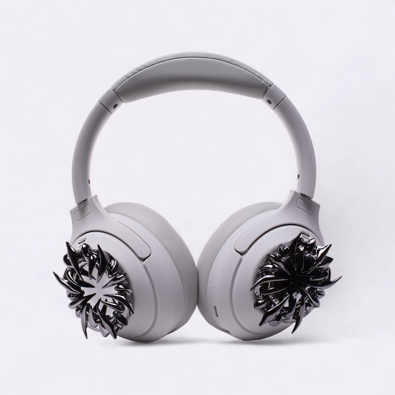 May include: Gray wireless headphones with black metal accents on the earcups. The accents are in the shape of a stylized starburst.