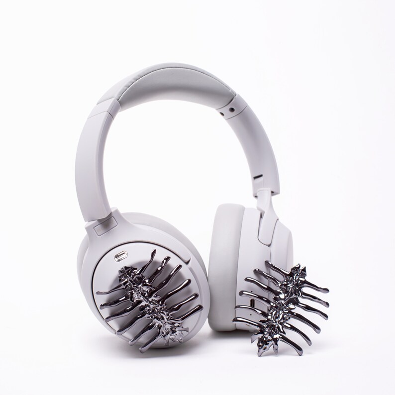 May include: A pair of white wireless headphones with a decorative black metal hair clip on each earcup.