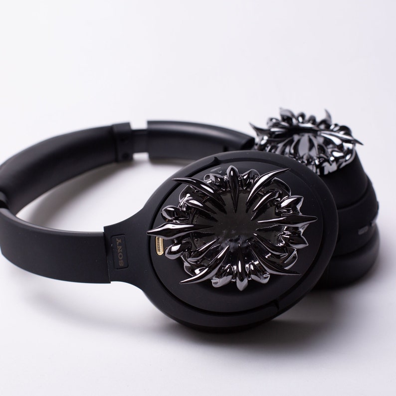 May include: Black over-ear headphones with a decorative, black metal design on the earcups. The headphones have the word "SONY" printed on the side.