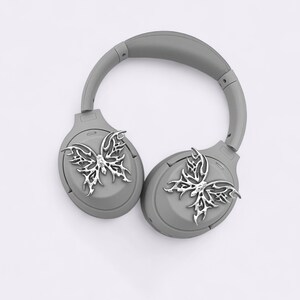 May include: Gray wireless headphones with a silver butterfly design on each earcup.