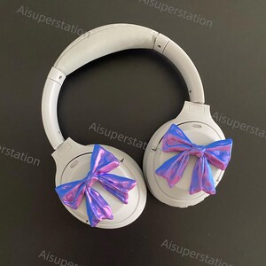 May include: White wireless headphones with a blue and purple iridescent bow on each earcup.