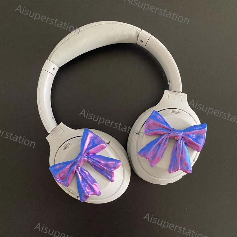May include: White wireless headphones with a blue and purple iridescent bow on each earcup.