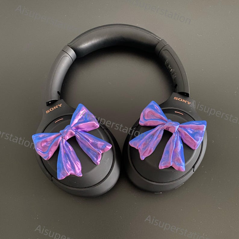 May include: Black over-ear headphones with a pink and blue iridescent bow on each earcup. The headphones have the word "SONY" printed on each earcup.