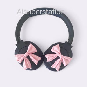Pode incluir: Fones de ouvido sem fio pretos com laços rosa presos a cada fone de ouvido.