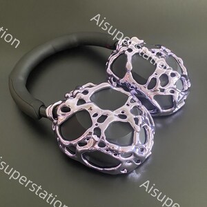 May include: A pair of black headphones with silver earcups. The earcups have a unique, textured design that resembles melted metal.