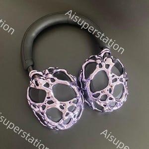 May include: A pair of silver headphones with a unique, textured design. The headphones have a black headband and earcups.