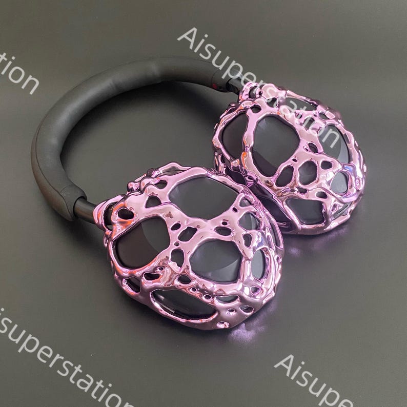May include: A pair of pink headphones with a textured, metallic finish. The headphones have a black headband and earcups.