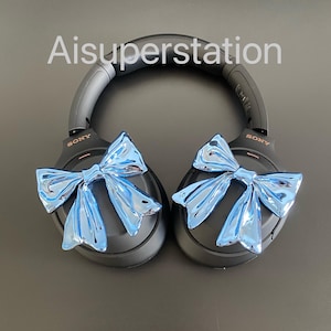 Pu&ograve; includere: Cuffie over-ear nere con fiocchi blu attaccati a ciascun padiglione. Le cuffie hanno la scritta "SONY" stampata su ciascun padiglione.