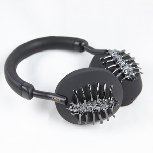May include: Black over-ear headphones with a unique design featuring a silver, skeletal-like pattern on each earcup. The headphones have a black leather headband and a gold "SONY" logo on the side.