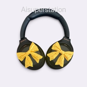 K&ouml;nnte beinhalten: Schwarze Over-Ear-Kopfh&ouml;rer mit gelben Schleifen an jedem Ohrpolster. Die Kopfh&ouml;rer tragen den Schriftzug "SONY" auf jedem Ohrpolster.