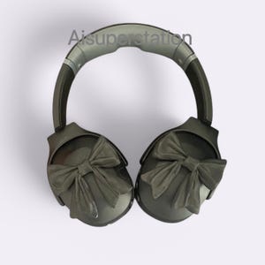 Pode incluir: Fones de ouvido pretos com faixa de cabeça cinza e laços pretos em cada fone de ouvido.