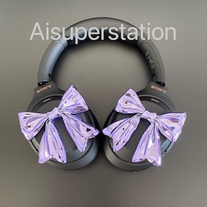Pu&ograve; includere: Cuffie over-ear nere con fiocchi viola attaccati a ciascun padiglione. Le cuffie hanno la scritta "SONY" stampata su ciascun padiglione.