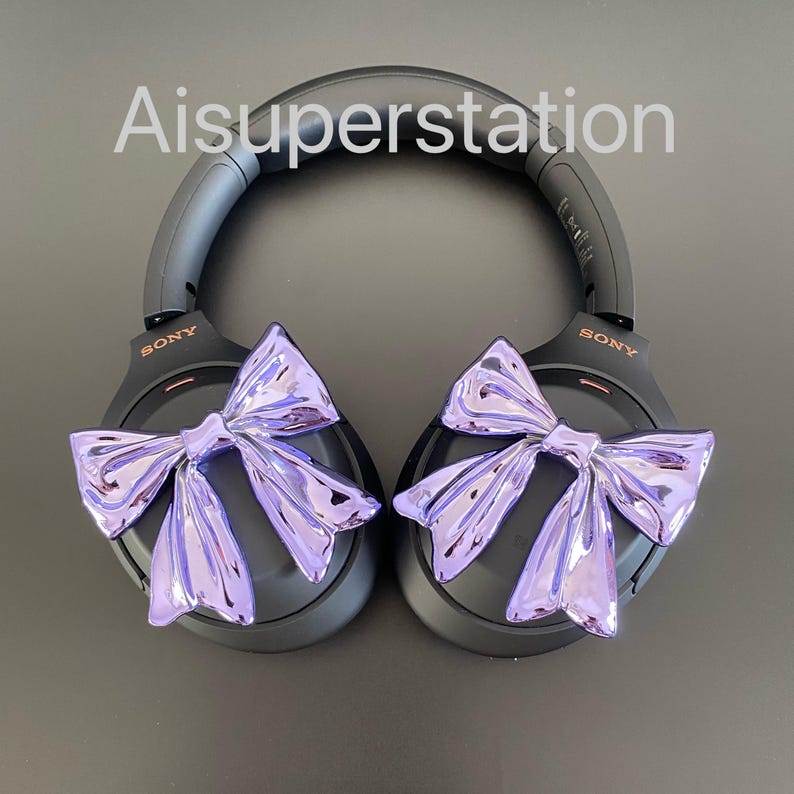 Pu&ograve; includere: Cuffie over-ear nere con fiocchi viola attaccati a ciascun padiglione. Le cuffie hanno la scritta "SONY" stampata su ciascun padiglione.