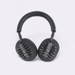 Puede incluir: Auriculares negros de diadema con un diseño decorativo plateado y negro en las almohadillas. Los auriculares tienen la palabra "SONY" escrita en el lateral.