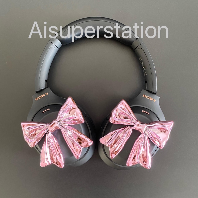 Pu&ograve; includere: Cuffie over-ear nere con fiocchi rosa attaccati a ciascun padiglione auricolare. Le cuffie hanno la scritta "SONY" stampata su ciascun padiglione auricolare.