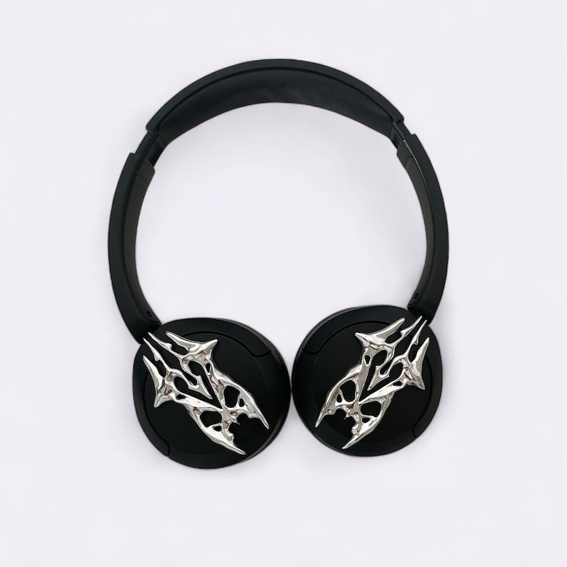 Puede incluir: Auriculares negros con dise&ntilde;os plateados de calavera en las almohadillas.