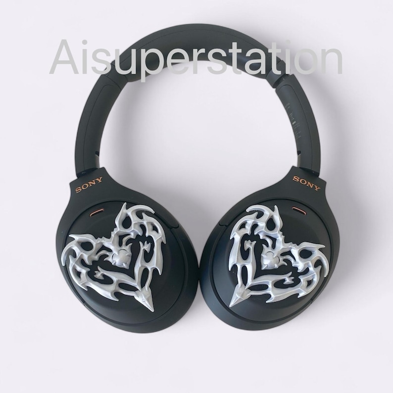 May include: Black over-ear headphones with a silver heart-shaped design on each earcup. The headphones have the word "SONY" printed on each earcup.