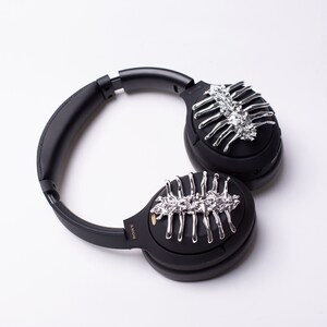 May include: Black over-ear headphones with silver decorative accents on each earcup. The accents resemble a skeletal structure.
