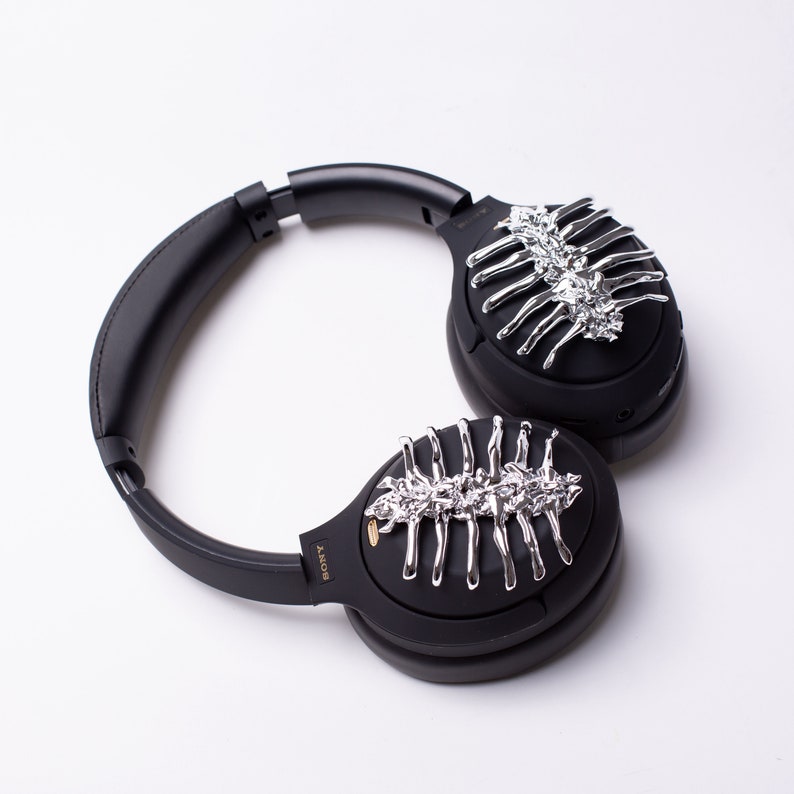 May include: Black over-ear headphones with silver decorative accents on each earcup. The accents resemble a skeletal structure.