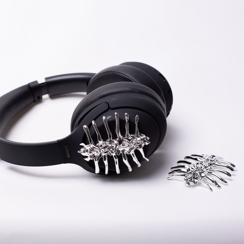 May include: Black over-ear headphones with a silver skeletal design on the earcup. A second silver skeletal design is shown separately.