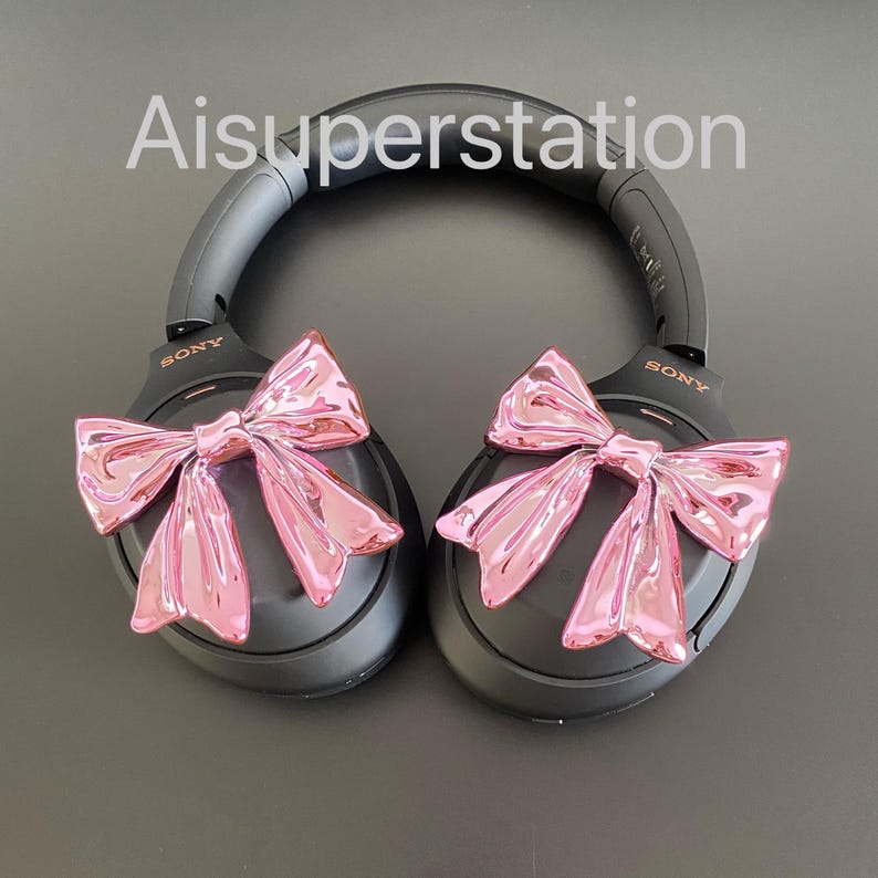 Pu&ograve; includere: Cuffie over-ear nere con fiocchi rosa attaccati a ciascun padiglione. Le cuffie hanno la scritta "SONY" stampata su ciascun padiglione.