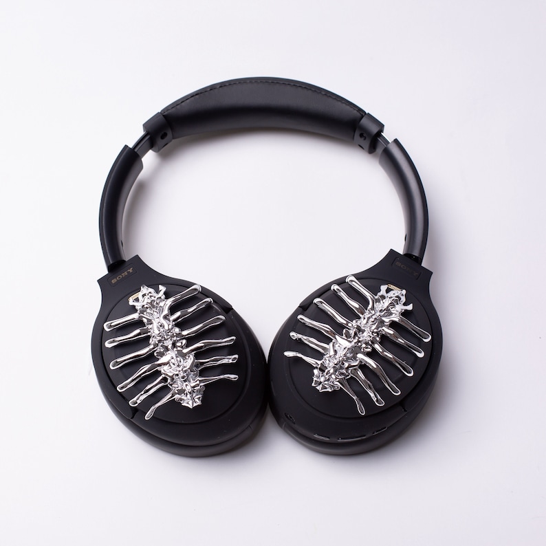 May include: Black over-ear headphones with a silver skeletal design on each earcup. The headphones have a black headband and the word "SONY" is printed on the left earcup.