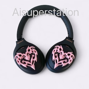 May include: Black over-ear headphones with pink heart-shaped designs on each earcup. The headphones have the word "SONY" written on each earcup.