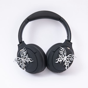 May include: Black wireless headphones with silver butterfly embellishments on each earcup. The headphones have a black headband and earcups with the word "SONY" printed on each side.