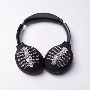 May include: Black wireless headphones with a silver skeleton design on each earcup.