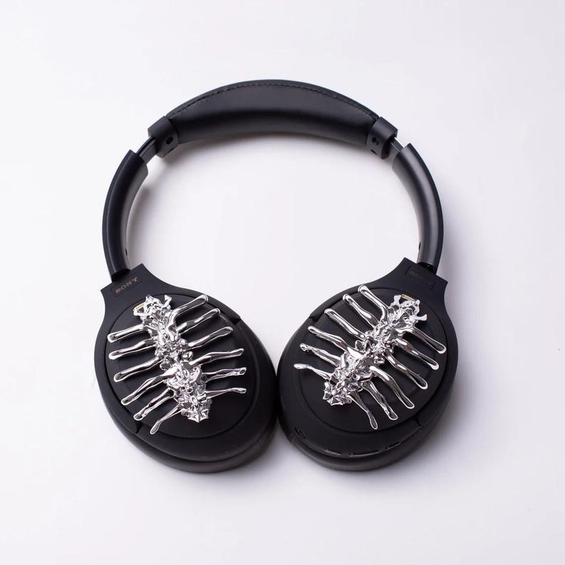 May include: Black wireless headphones with a silver skeleton design on each earcup.