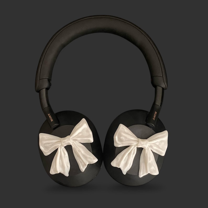 K&ouml;nnte beinhalten: Schwarze Over-Ear-Kopfh&ouml;rer mit wei&szlig;en Schleifen an jedem Ohrpolster. Die Kopfh&ouml;rer haben den Schriftzug "SONY" an der Seite.