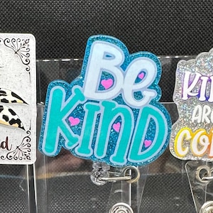 May include: Three badge reels with positive messages. One has a sunflower with the words "Be Kind". Another says "Be Kind" with hearts. The third says "Throw Kindness Around Like Confetti".